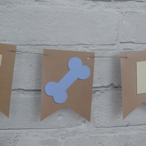 May include: A brown paper banner with the word "IT" in yellow letters and a blue bone shape in the center. The banner is strung with twine.