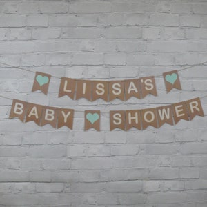 May include: A brown paper banner with the text "Lissa's Baby Shower" in white letters. The banner is decorated with blue hearts.