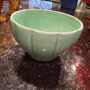 May include: A light mint green ceramic bowl featuring a scalloped exterior design with vertical ridges and a smooth, rounded rim. The bowl has a consistent pastel green glaze throughout its interior and exterior surface, showcasing a simple, functional form.