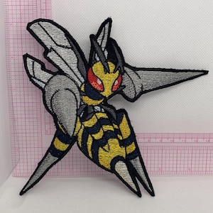 May include: An embroidered patch featuring a stylized insectoid creature with yellow and black striped segments, grey wings, and red eyes. The patch is positioned against a clear plastic ruler showing a width of approximately 5.5 inches.