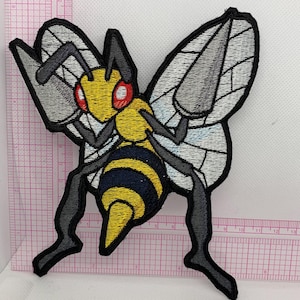 May include: An embroidered patch of a stylized insect with a yellow head, red eyes, and a black and yellow striped abdomen. The creature has grey wings and long, dark grey legs. A pink grid ruler is visible behind the patch, showing it is approximately 5 inches tall and 5 inches wide.
