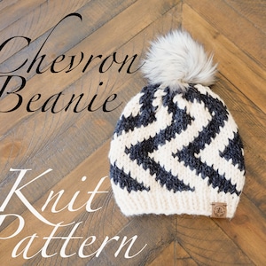 May include: Black and white chevron knit beanie with a faux fur pom pom on top. The beanie is lying on a wooden surface.  Chevron Beanie Knit Pattern.