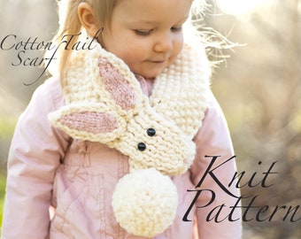 May include: A white and pink knitted bunny scarf with black button eyes and a white pom-pom tail. The scarf is worn by a child and the text "Cotton Tail Scarf Knit Pattern" is visible in the image.