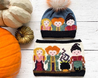 Puede incluir: Un gorro azul de punto con un pompón blanco y una imagen bordada de colores de las hermanas Sanderson de la película Hocus Pocus. El gorro se combina con una bufanda blanca de punto a juego con una imagen bordada similar de las hermanas Sanderson.