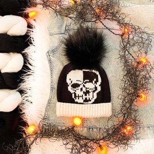 Può includere: Un cappello di lana nero e bianco con un pon pon nero. Il cappello è appoggiato su una giacca di jeans con un bordo di pelliccia bianca.
