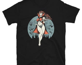 May include: A black t-shirt with a graphic of a woman with red hair and a red cape standing in front of a full moon. The woman is wearing a red and white outfit and has a red cape. The moon is surrounded by bats.
