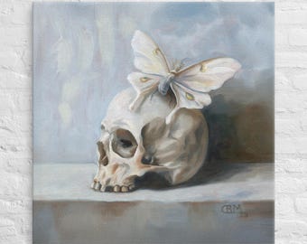 May include: An oil painting depicts a human skull with a large white moth perched on top. The moth has delicate wings with yellow markings. The artwork is set against a soft, muted background with a signature in the bottom right corner.