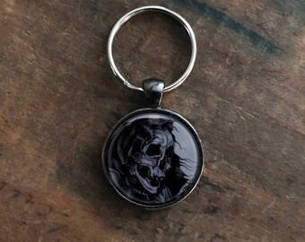 May include: A silver key chain with a black and white round charm featuring a skull design.