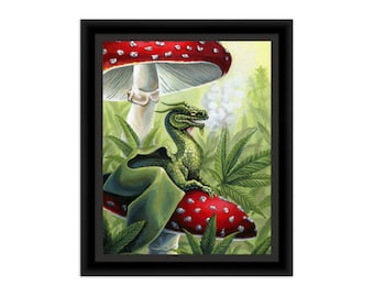 May include: A framed art print featuring a green dragon with scales sitting atop a red mushroom with white spots. The dragon exhales a puff of white smoke. The background consists of green serrated leaves, and the entire scene is enclosed in a black frame.