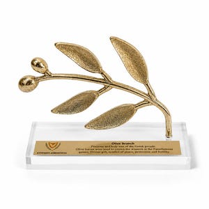 May include: A gold-colored metal olive branch sculpture with two olives and five leaves, mounted on a clear rectangular acrylic base. A gold plaque on the base features the text: Olive Branch, Precious and holy tree of the Greek people.