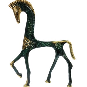 May include: A stylised metal horse figurine featuring a dark green patina finish with polished gold-tone accents on the mane, face, hooves, and tail. The body is decorated with engraved floral patterns and geometric Greek key motifs along the neck.