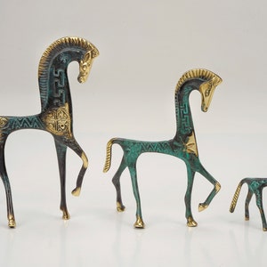 May include: Three horse figurines of varying sizes crafted from metal with a dark green patina and polished gold-tone accents. Each horse features a stylised mane, a slender body, and intricate geometric patterns engraved along the neck and torso.
