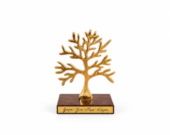 May include: A gold-colored metal tree sculpture with a textured finish, mounted on a rectangular dark brown wooden base. A small gold plaque on the front of the base features the Greek text: Agapi - Ygeia - Chara - Eftychia in black script.