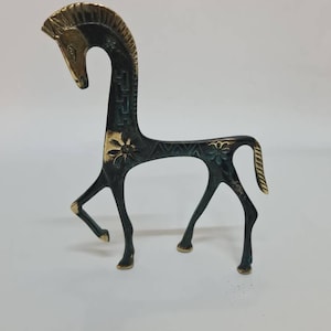 May include: A stylised metal horse figurine featuring a dark, oxidised finish with polished gold-tone accents on the mane, face, and tail. The body is decorated with engraved floral patterns and geometric lines, standing on four slender legs.