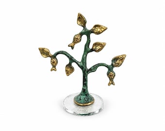 May include: A decorative tree sculpture featuring a textured, oxidized green trunk and branches with polished gold-toned leaves and small fruit-like accents. The sculpture is mounted on a clear, circular acrylic base for stability.