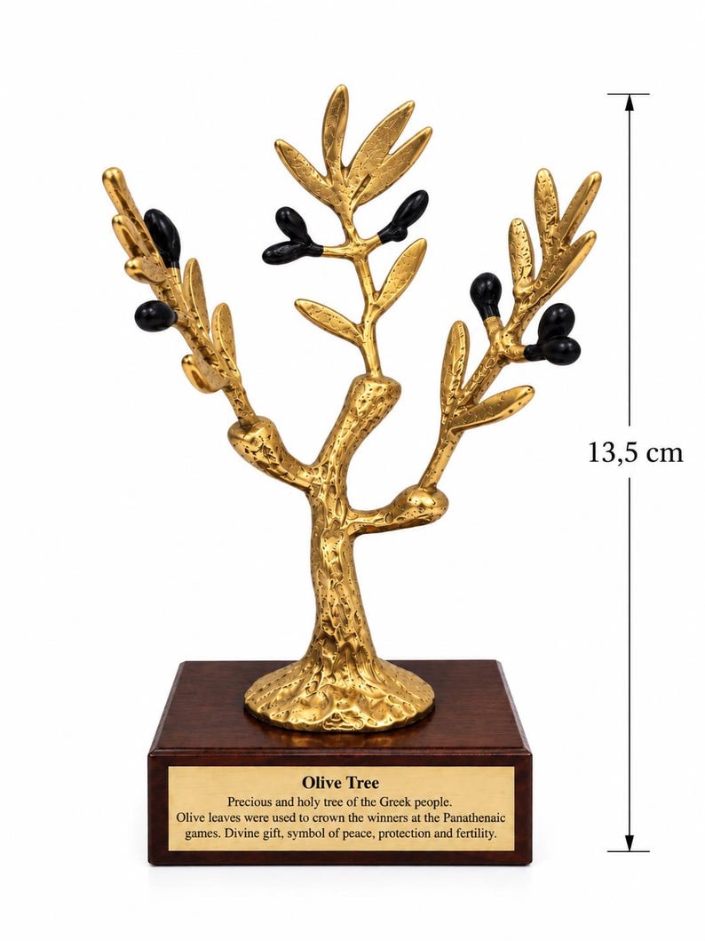 May include: A gold-colored olive tree sculpture with black olives, mounted on a square wooden base. A plaque on the base reads: Olive Tree, Precious and holy tree of the Greek people. Olive leaves were used to crown the winners at the Panathenaic games, Divine gift, symbol of peace, protection and fertility. Height is 13.5 cm.