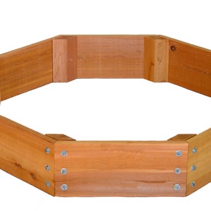 May include: Octagonal wooden raised garden bed with a natural wood finish. The bed is made of cedar wood and has a simple design.