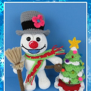 Peut inclure: Un bonhomme de neige en crochet tenant un balai et debout à côté d'un sapin de Noël en crochet avec une étoile au sommet. Le bonhomme de neige porte un chapeau haut de forme noir et gris avec une fleur rose, une écharpe rouge et verte, et a un nez rouge et une bouche bleue.