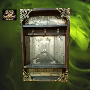 Puede incluir: Un porta llaves de madera con un aspecto vintage, que presenta una imagen del pasillo de la película "El Resplandor". El texto "Grand Overlook Hotel" y "Redrum" son visibles en el porta llaves.