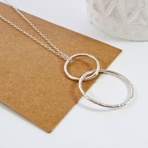 May include: A silver necklace with two interlocking circles. The circles are textured and have a hammered finish.