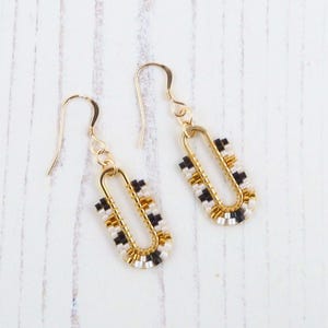 May include: A pair of gold hoop earrings with black and white beads. The earrings are made of small, square beads that are arranged in a geometric pattern.