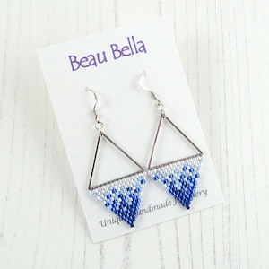 May include: A pair of silver triangle earrings with blue and white beaded fringe. The earrings are displayed on a white card with the text "Beau Bella Unique Handmade Jewellery".