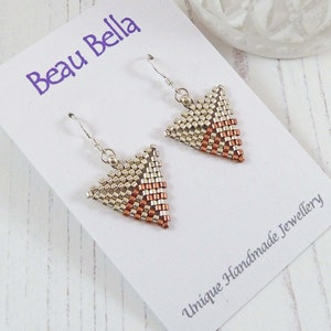May include: A pair of silver and copper triangle earrings with a geometric pattern. The earrings are on a white card with the text "Beau Bella" and "Unique Handmade Jewellery".