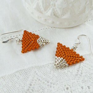 May include: A pair of orange and silver triangle shaped earrings with silver hooks. The earrings are made of small beads.
