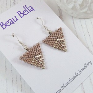 May include: A pair of triangle-shaped earrings with a silver hook and a beige and gold beaded design. The earrings are displayed on a white card with the text "Beau Bella" and "Unique Handmade Jewellery".