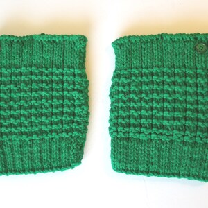 May include: A pair of green knitted leg warmers with a button on each. The leg warmers are made with a textured stitch.