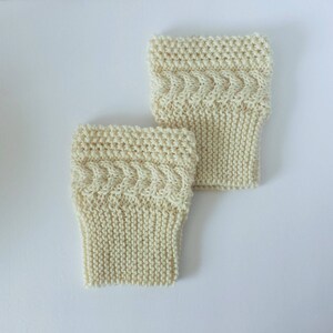 May include: A pair of cream-colored knitted leg warmers with a cable knit pattern.