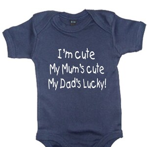 Może przedstawiać: Granatowy śpioszek dla niemowlęcia z białym napisem "I'm cute My Mum's cute My Dad's Lucky!"