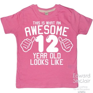 Può includere: Maglietta rosa con testo bianco che dice "This is what an awesome 12 year old looks like" con due pollici in su su entrambi i lati del numero 12.