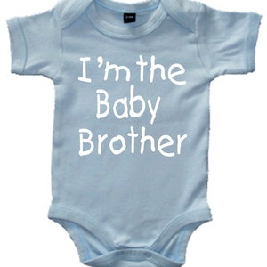 Może przedstawiać: Jasno niebieski śpioszek dla niemowlęcia z białym napisem "Jestem młodszym bratem".