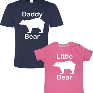 May include: A navy blue t-shirt with the text "Daddy Bear" and a white polar bear silhouette. A pink t-shirt with the text "Little Bear" and a white polar bear silhouette.
