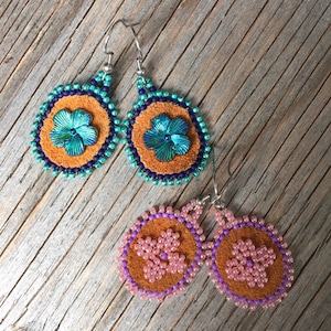 Può includere: Due paia di orecchini con perline e retro in pelle. Un paio ha perline turchesi e viola con un fiore turchese, l'altro paio ha perline rosa e viola con un fiore rosa.