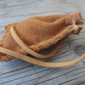 Peut inclure: Une petite bourse en cuir marron avec une fermeture à cordon et un détail de frange. La bourse est faite de cuir souple et doux et a un aspect rustique et fait main.