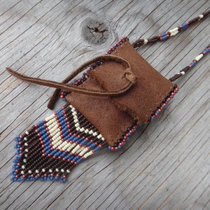 Peut inclure: Une bourse en cuir marron avec une frange perlée et un cordon perlé. La bourse est décorée de perles bleues, blanches et brunes.