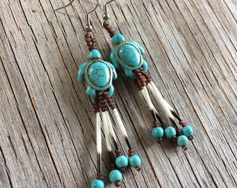 Puede incluir: Pendientes de tortuga turquesa con detalles marrones y blancos. Los pendientes presentan colgantes de tortuga turquesa, cuentas marrones y hebras blancas similares a púas, creando un diseño único inspirado en la naturaleza.