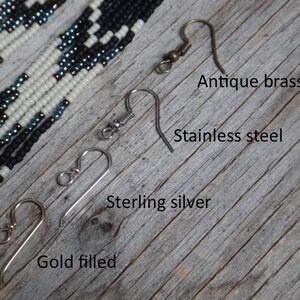 May include: Four different earring hooks are shown on a wooden surface. The hooks are labeled "Antique brass", "Stainless steel", "Sterling silver", and "Gold filled".
