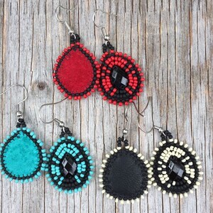 Puede incluir: Tres pares de pendientes de cuentas con detalles de cuero. Los pendientes son de color rojo, turquesa y negro con cuentas negras y una piedra preciosa negra en el centro.