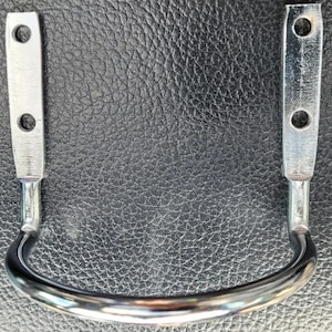 May include: A silver metal hook with two holes on each side. The hook is curved and has a smooth finish.