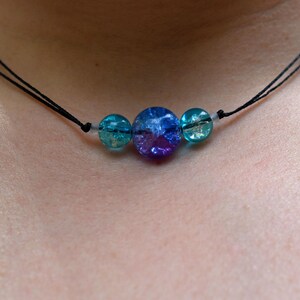 May include: A simple necklace with three round glass beads. The beads are blue, purple, and green. The necklace is made with black cord.