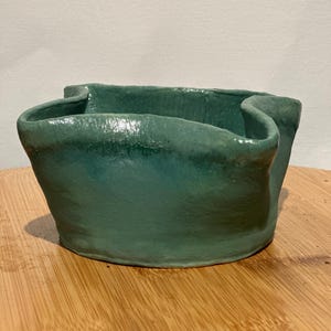 Può includere: Una ciotola in ceramica turchese fatta a mano con un esclusivo bordo ripiegato. La ciotola ha una base arrotondata e una superficie strutturata, che mostra il tocco dell'artigiano. La glassa turchese aggiunge un tocco di eleganza a questo pezzo d'arte funzionale.