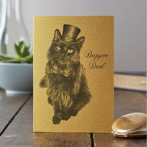 May include: A gold card featuring a black and white illustration of a cat wearing a top hat, bow tie, and monocle. The text "Dapper Dad" is printed on the card.