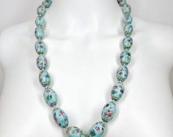 May include: A long necklace made of oval-shaped porcelain beads. The beads are painted with a light blue background and floral designs in pink, green, and yellow.
