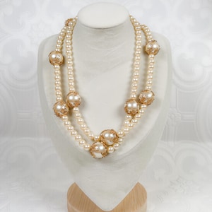 May include: A double strand pearl necklace with gold accents. The necklace features large, round pearls with intricate gold designs.