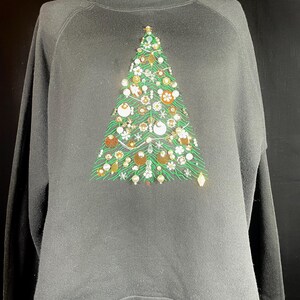 May include: Black sweatshirt with a green Christmas tree design embellished with sequins, beads, and other decorative elements.