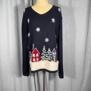 May include: A navy blue V-neck sweater featuring a winter scene with a white snowy base, two houses in red and blue, green pine trees, and white embroidered snowflakes scattered across the upper portion of the garment and long sleeves.