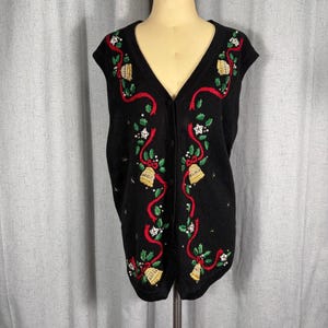 May include: A black sleeveless knit vest featuring a V-neckline and a button-down front. The garment is decorated with embroidered gold bells, red ribbons, green holly leaves, and white star accents arranged in a festive holiday pattern.